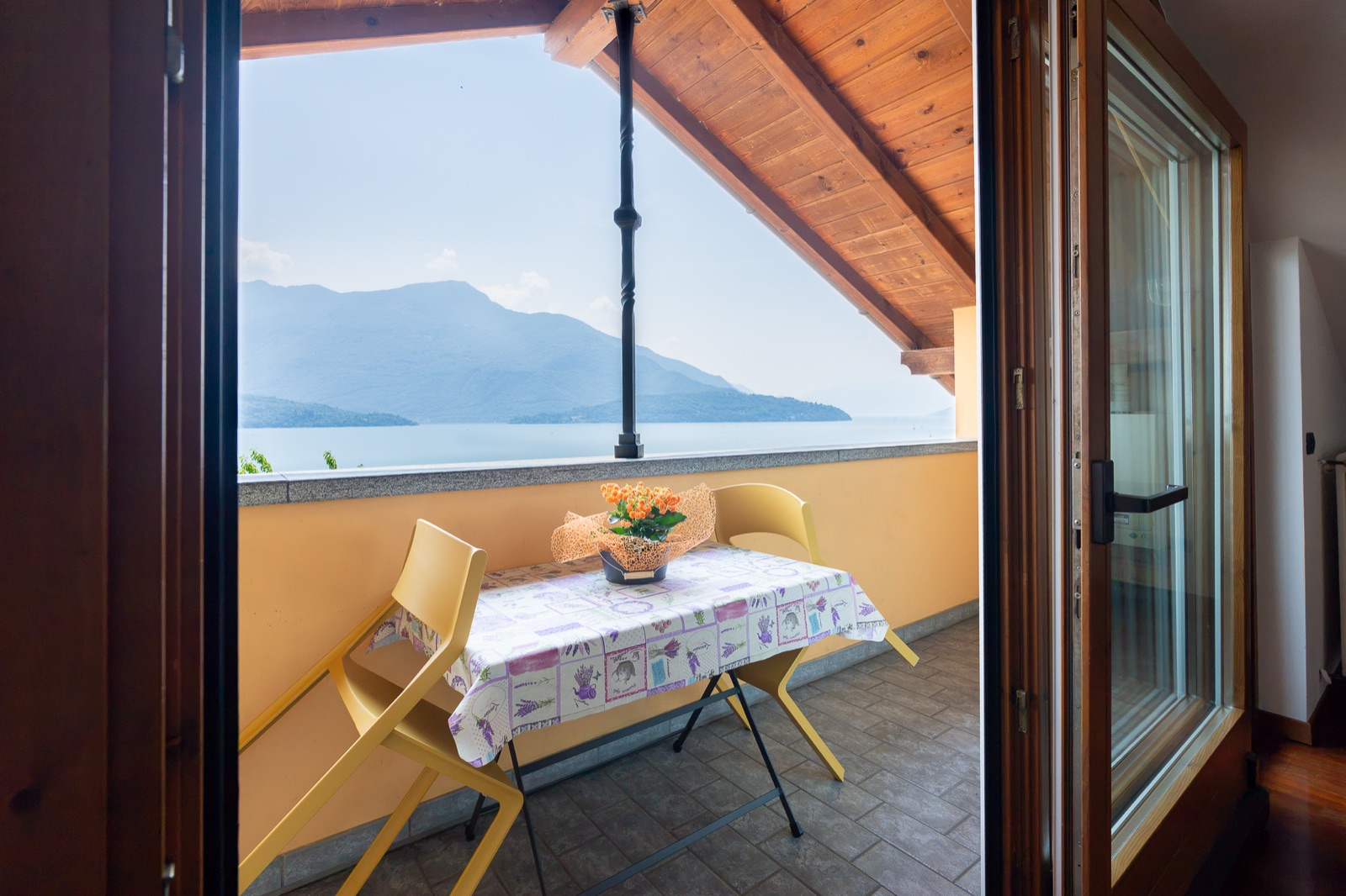 Überdachte Terrasse mit kleinem Tisch, gelben Stühlen und Seeblick